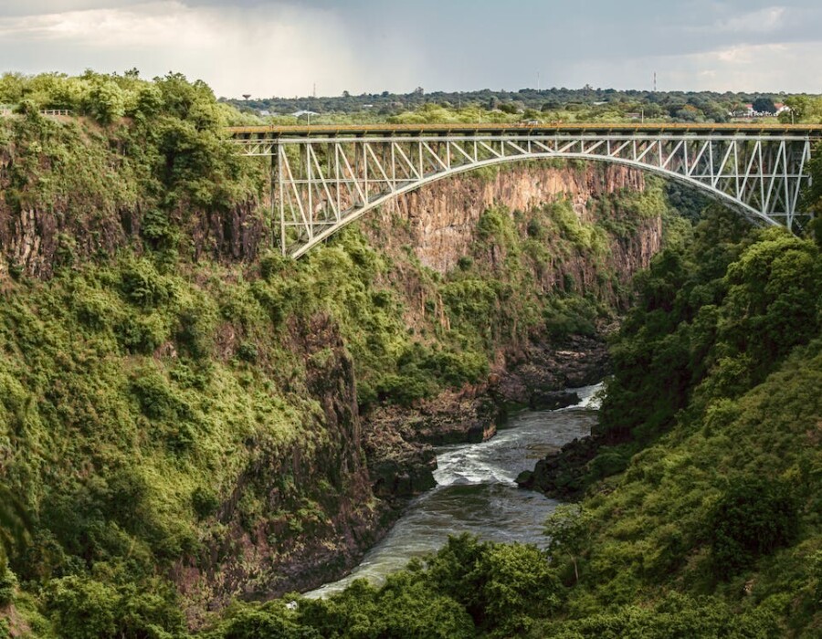 A steel bridge over a river in a mountain area with many trees.