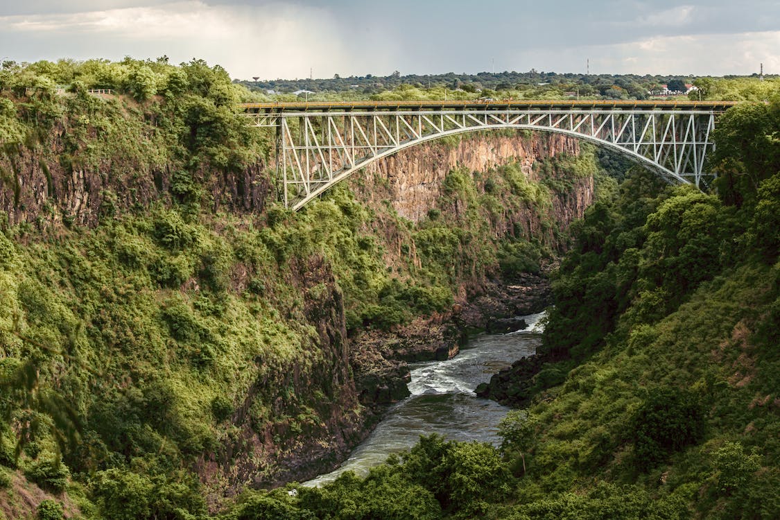 A steel bridge over a river in a mountain area with many trees.