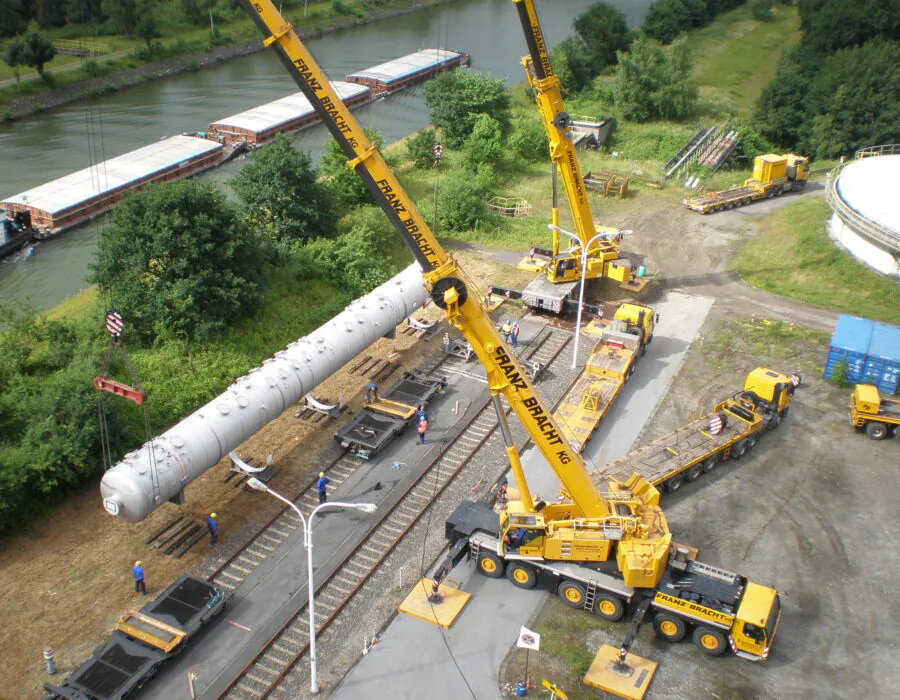 A yellow crane lifting goods onto a railway cart beside a river